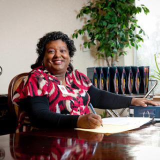 A woman smiles while writing at her desk in a professional office setting.