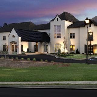 A luxurious mansion illuminated in the evening with a well-manicured lawn.