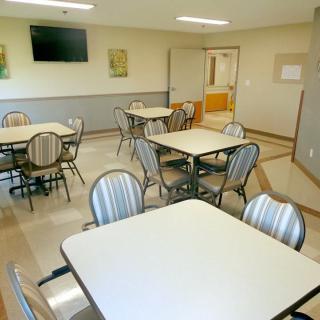 An empty dining room with multiple tables and chairs, featuring a wall-mounted television.