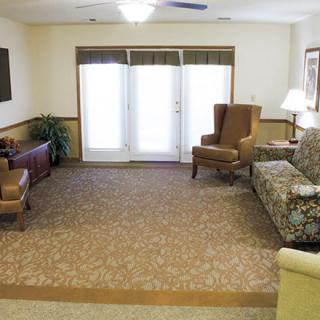 A cozy living room with various pieces of furniture including sofas and chairs, all arranged on a carpeted floor with large windows in the background.