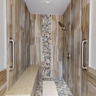 A modern shower with wood-like tiles, featuring a pebble accent strip and built-in bench.
