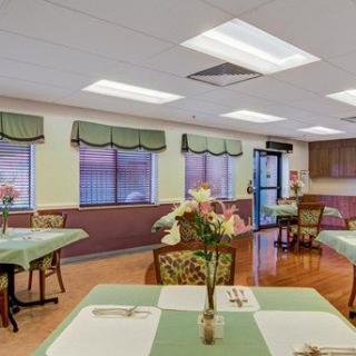 A cozy dining room with neatly arranged tables and chairs, featuring floral decorations and natural lighting.