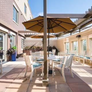 A sunny patio with tables, chairs, and umbrellas in a courtyard setting.
