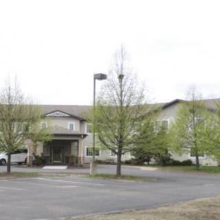 A large building with an entrance, surrounded by trees and a parking lot under an overcast sky.