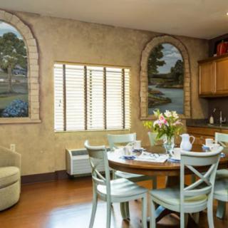 A cozy dining area with a round wooden table surrounded by chairs, featuring rural-themed wall art and a vase of flowers in the center.