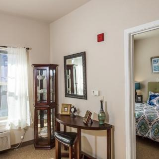 A cozy interior featuring a small desk, mirror, and a glimpse into a bedroom.