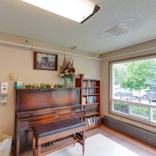 A cozy corner featuring a wooden piano, a bookshelf filled with books, and a window that allows natural light to flow in.