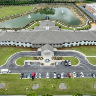 Aerial view of a large building with a curved driveway, surrounded by a parking lot and scenic landscape including a pond with fountains.