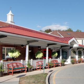 The entrance of a building with a red roof, featuring benches and hanging plants.