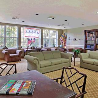 A spacious living room with comfortable seating, large windows, and a bookshelf.