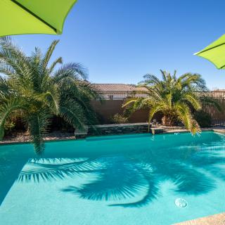 A serene outdoor swimming pool area with palm trees and umbrellas on a sunny day.