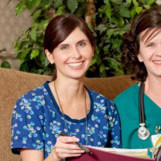 Two nurses in uniforms, smiling and holding medical files.