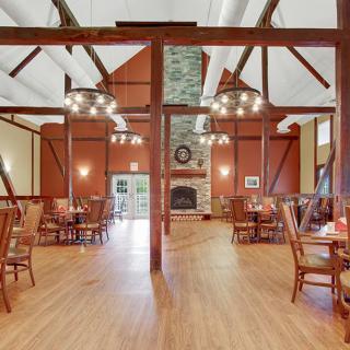 A spacious dining room with rustic wooden beams, chandeliers, and a central fireplace.
