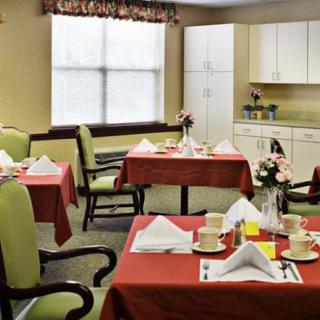 A cozy dining room with neatly set tables and chairs, featuring a small kitchen area.