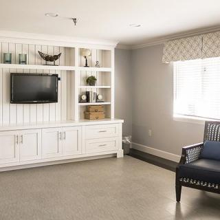 A modern living room with a built-in shelving unit featuring a mounted television and decorative items, alongside a comfortable armchair near the window.
