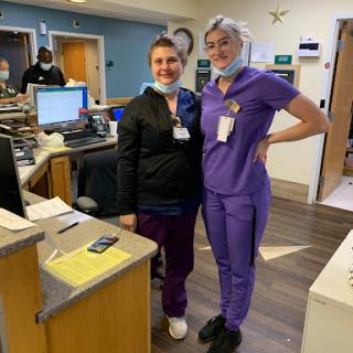 Two healthcare professionals posing together in a hospital setting, showcasing their scrubs and teamwork.