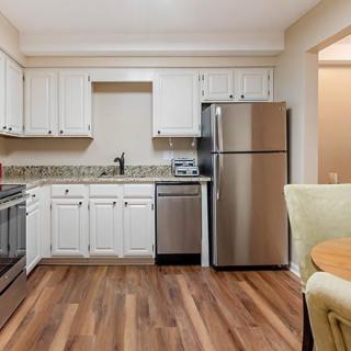 A modern kitchen with stainless steel appliances, white cabinets, and hardwood flooring.