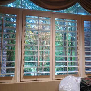 A view from inside looking out through wooden blinds, showcasing a serene natural landscape.