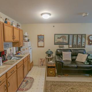 A cozy living area with an adjoining kitchen, featuring wooden cabinets and a comfortable couch.