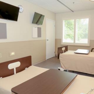 A clean and modern hospital room with two beds and wall-mounted televisions.