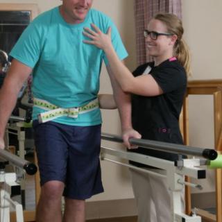 A healthcare professional assists a patient during physical therapy with a walking aid.