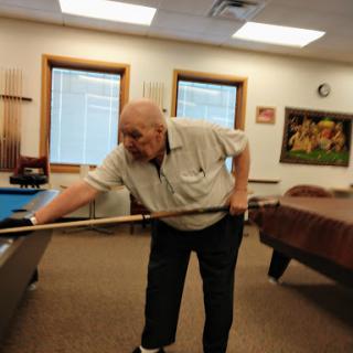 An elderly man focused on making a shot at the billiard table.