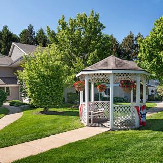 A charming suburban scene with a gazebo, lush green lawn, and surrounding houses on a sunny day.