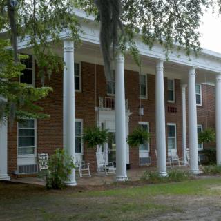 A historic brick building with large white columns on the porch, surrounded by trees.