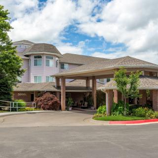 Exterior view of a building with a welcoming entrance and landscaped surroundings under a cloudy sky.