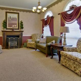A traditional living room with elegant furnishings, featuring a fireplace and large windows with draped curtains.