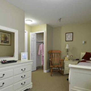 A cozy bedroom featuring a white dresser with a mirror, a rocking chair, and an open closet.