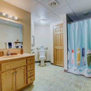 A well-lit bathroom featuring a wooden vanity, mirror, toilet, and a colorful shower curtain.