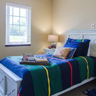 A cozy bedroom featuring a single bed with colorful bedding, a nightstand with a lamp, and books neatly placed on the bed.
