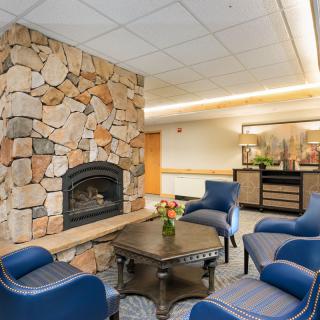 A cozy lounge area with a stone fireplace and blue chairs arranged around a central table.