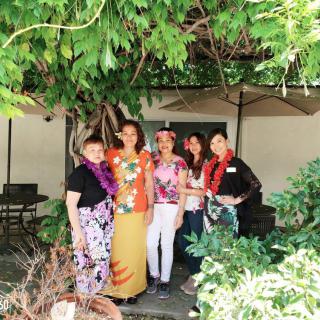 A group of people smiling and standing together outdoors, surrounded by lush greenery.