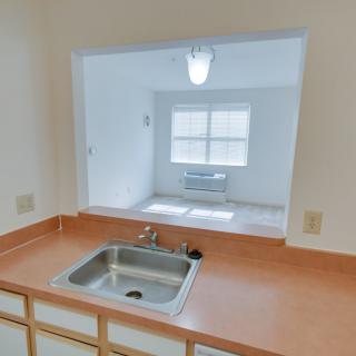 A view from the kitchen through an open space, featuring a sink and countertop.