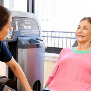 A woman exercising with the assistance of a trainer in a gym.