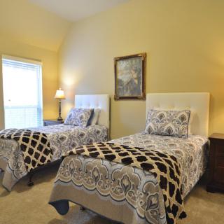A cozy bedroom featuring two twin beds with patterned bedding, a bedside lamp, and wall art.