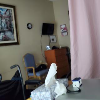 A view of a hospital patient room featuring a curtain for privacy, a chair, and some tissues on a table.