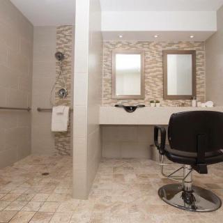 A modern accessible bathroom with a vanity area, mirrors, and a tiled shower space.
