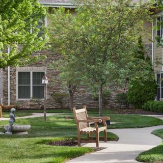 A peaceful garden area with a bench and walkway surrounded by trees and grass.