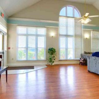A spacious living room with large arched windows and abundant natural light, featuring wood flooring and a vaulted ceiling.