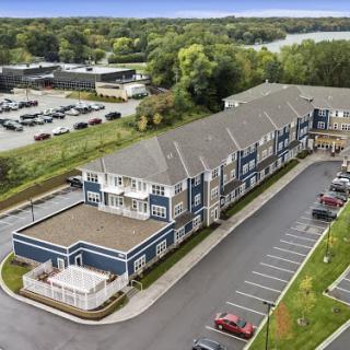 Aerial view of a large residential building with an adjacent parking lot and surrounding greenery.