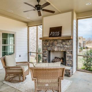 A cozy outdoor patio with woven furniture, a stone fireplace, and a ceiling fan.