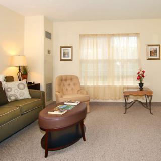 A cozy living room with a sofa, armchair, and coffee table in front of a curtained window.