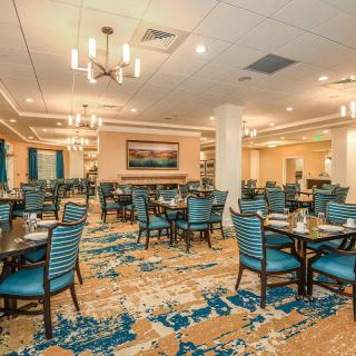 A spacious and elegantly decorated dining area with tables set for service, featuring modern lighting and a colorful carpet.