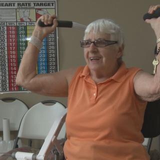 A senior woman smiling while lifting dumbbells in an exercise class.