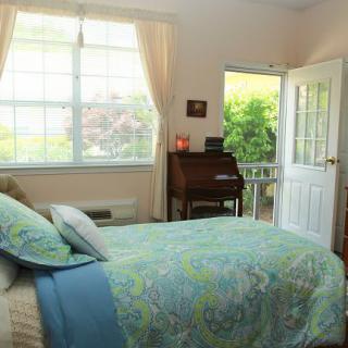 A cozy bedroom with a bed, desk, and open door leading to a garden.