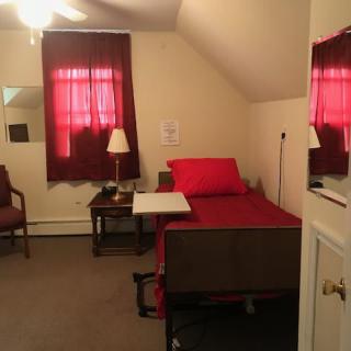 A small, neatly arranged bedroom with a bed, nightstand, and chair.