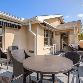 A sunny patio area with outdoor furniture, including a dining table and chairs, attached to a house.
